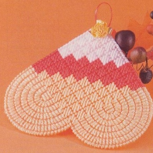 May include: A heart-shaped crocheted ornament with a pink, white, and red striped pattern. The ornament is made with a light orange yarn and has a loop at the top for hanging.