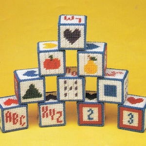 May include: A stack of colorful fabric blocks with different letters, numbers, and shapes. The blocks are made of canvas and have a blue border. The blocks are arranged in a pyramid shape.