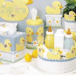 May include: A collection of baby-themed items featuring a yellow duckling motif. Includes a tissue box, a container, a basket, and decorative ducklings. The color palette is soft, with yellow, blue, and white, creating a cheerful and inviting aesthetic.