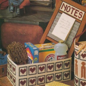 Puede incluir: Una cesta rectangular blanquecina con un patrón repetido de corazones rojos en cuadrados negros. La cesta contiene un cepillo, productos de limpieza y una botella. Un bloc de notas enmarcado con la palabra "NOTES" está en el fondo.