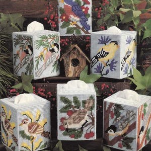 May include: Set of seven tissue box covers featuring colorful embroidered bird designs. Each cover has a different bird and floral pattern, including a bluebird, a yellow bird, and a brown bird.