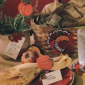 May include: A Thanksgiving table setting with a woven basket, bread, and a decorative turkey. A napkin is held by a pumpkin-shaped napkin ring. A small card reads "John". A list of Thanksgiving foods is visible.