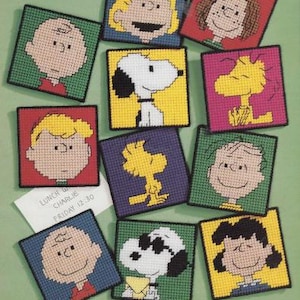 May include: A set of 10 colorful square-shaped plastic canvas needlepoint patterns featuring characters from the Peanuts comic strip. The characters include Charlie Brown, Snoopy, Lucy, Linus, and Woodstock. The patterns are ready to be stitched.
