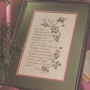 May include: A cross-stitch pattern with a floral design and the text "The Lord's Prayer" and the words of the prayer. The prayer is written in a cursive font and the flowers are in shades of green, pink, and white.