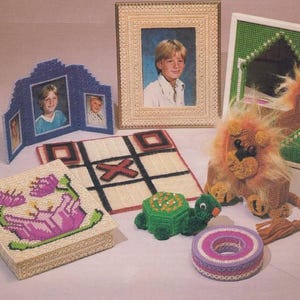 May include: A collection of handmade crafts, including framed photos, a tic-tac-toe board, a decorative box with a floral design, a turtle, a lion, and a circular object. The crafts are made with yarn.