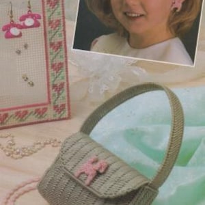 May include: A gray plastic purse with a pink flower design. The purse has a shoulder strap and a flap closure. There are also pink plastic earrings and a necklace in the image.