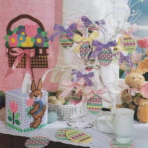 May include: A set of Easter-themed cross-stitch crafts, including a basket of flowers, a bunny tissue box cover, and egg-shaped ornaments. The ornaments are hanging from a white branch with purple and pink ribbons.