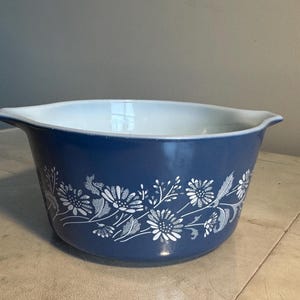 May include: A blue mixing bowl with a white floral design. The bowl has a white interior and a dark blue exterior. The floral pattern includes stylized flowers and leaves. The bowl has two handles.