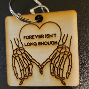Puede incluir: Llavero de madera con un corazón y dos manos de esqueleto que se agarran. El corazón tiene el texto "FOREVER ISN'T LONG ENOUGH".