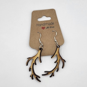 May include: A pair of wooden antler earrings with silver hooks. The earrings are on a brown card with the text "Handmade with love".