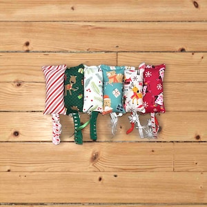 May include: Six rectangular fabric cat toys featuring various holiday patterns including red and white candy cane stripes, reindeer on green, pine branches, cats with gifts, festive deer, and penguins on red, each with a dangling ribbon.