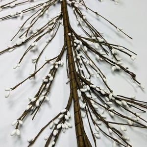 May include: A brown twig Christmas tree with white berry-like decorations. The tree is made of multiple twigs that are bundled together to form a tree shape. The twigs are covered in small white berries.