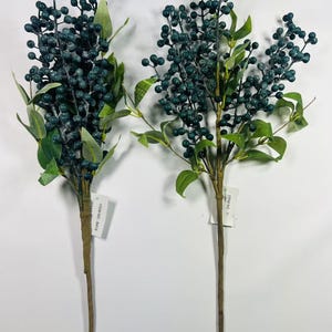 May include: Two sprigs of artificial greenery with blue berries. The sprigs are tied together with twine and have a white tag with the text "ITEM NO. 8314" on each.