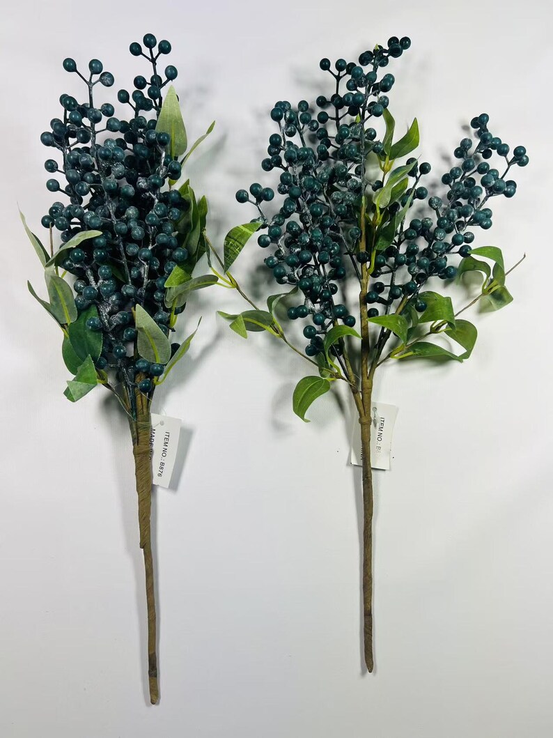 May include: Two sprigs of artificial greenery with blue berries. The sprigs are tied together with twine and have a white tag with the text "ITEM NO. 8314" on each.