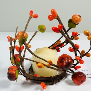 May include: A brown twig wreath with orange and red berries and faux pumpkins, designed to hold a candle. The wreath is made of natural materials and has a rustic look. The text "ITEM NO. CY092-1 CHINA" is visible on the bottom right corner of the image.