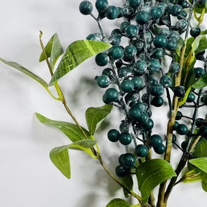 May include: A sprig of faux greenery with dark green leaves and frosted dark green berries.
