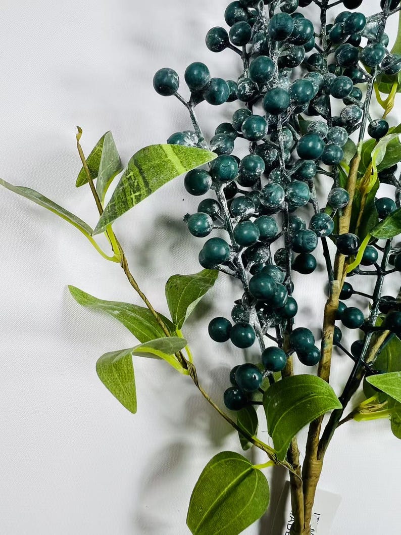 May include: A sprig of faux greenery with dark green leaves and frosted dark green berries.
