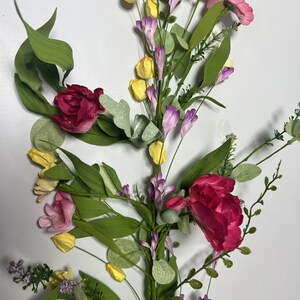 May include: A floral garland with pink, red, and yellow flowers, green leaves, and purple accents. The garland is perfect for adding a touch of spring to your home decor.