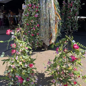May include: Two metal stands decorated with pink and purple artificial flower garlands. The garlands are made of silk flowers and greenery.