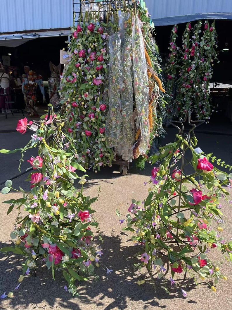 May include: Two metal stands decorated with pink and purple artificial flower garlands. The garlands are made of silk flowers and greenery.