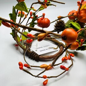 May include: A brown twig wreath with orange and red berries and green leaves. The wreath has a tag attached that says "ITEM NO. G1904-2 MADE IN CHINA".
