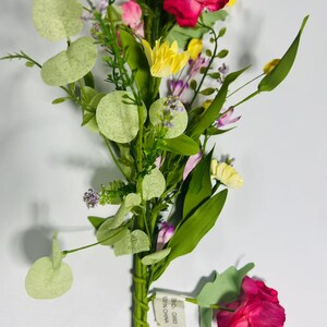 May include: A bouquet of artificial flowers with pink, yellow, and purple blooms. The bouquet is made of silk flowers and has a green stem. The flowers are arranged in a cluster and have a realistic appearance. The bouquet is tied with a green ribbon and has a tag that says "Made in China".