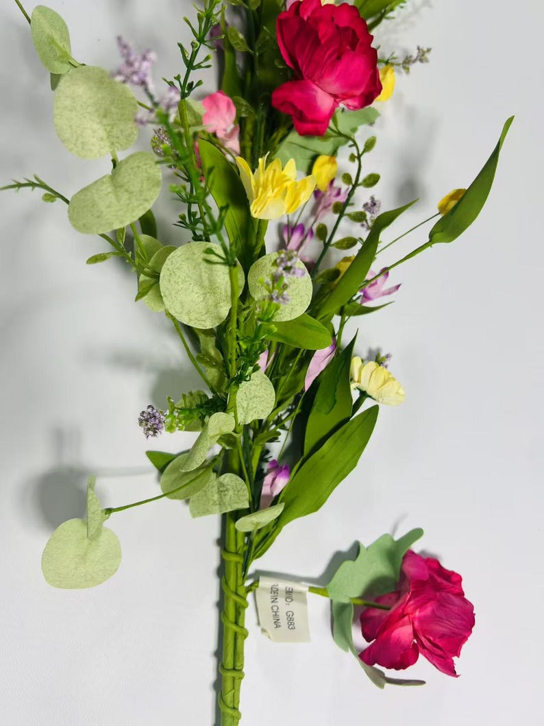 May include: A bouquet of artificial flowers with pink, yellow, and purple blooms. The bouquet is made of silk flowers and has a green stem. The flowers are arranged in a cluster and have a realistic appearance. The bouquet is tied with a green ribbon and has a tag that says "Made in China".