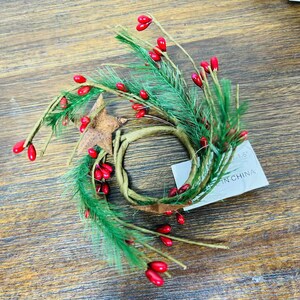 May include: A green and brown wreath with red berries. The wreath is made of pine branches and has a brown twine center. The tag attached to the wreath reads "1.5" and "Made in China".