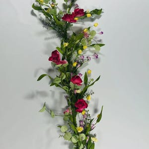 May include: A long garland of artificial flowers with pink roses, yellow and purple wildflowers, and green leaves.
