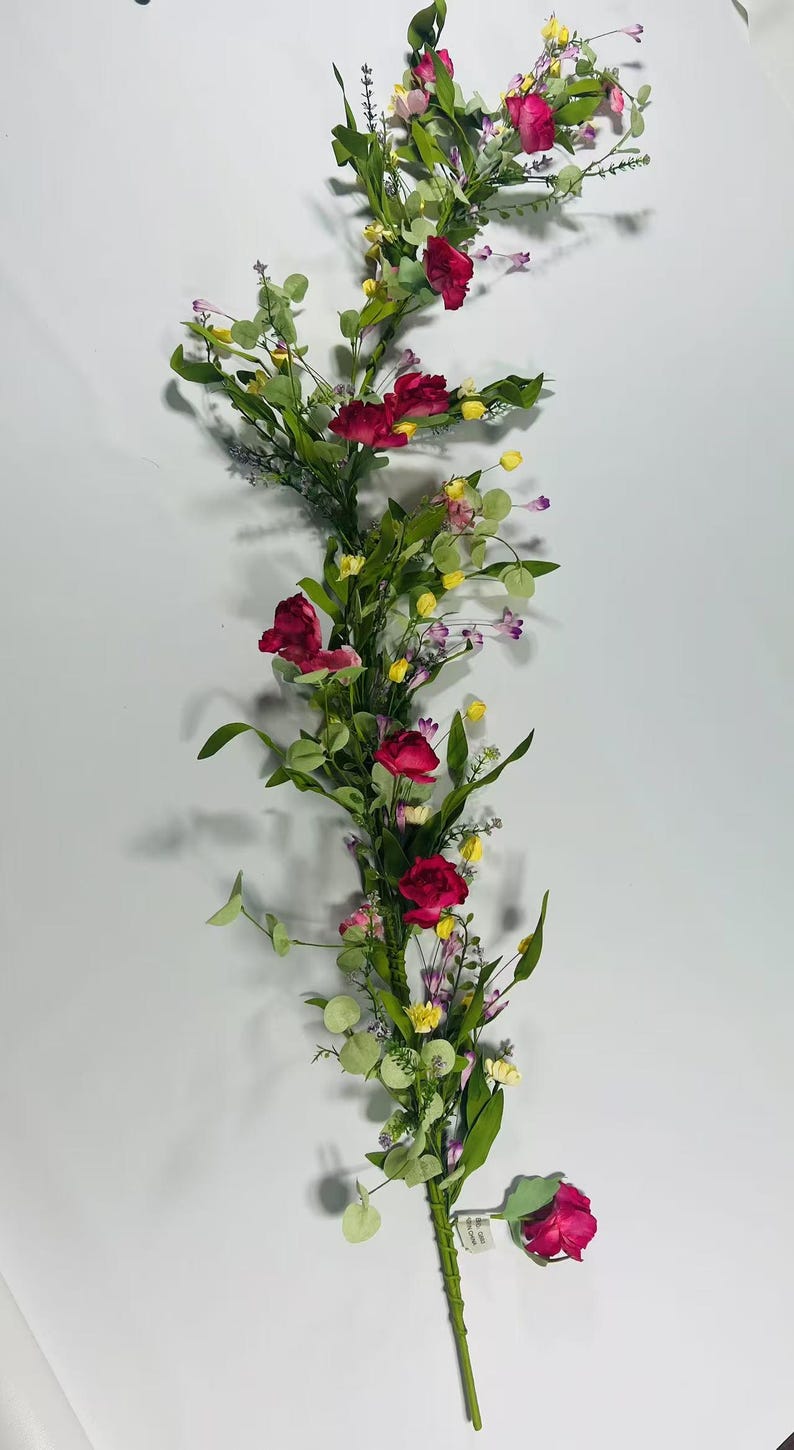 May include: A long garland of artificial flowers with pink roses, yellow and purple wildflowers, and green leaves.