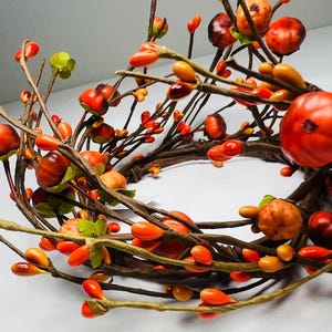 May include: A brown twig wreath with orange and red berry accents. The wreath is made of natural twigs and has a rustic look.
