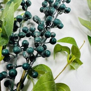 May include: A sprig of faux greenery with dark green berries and leaves. The berries have a frosted finish.