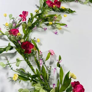May include: A pink and green floral garland with small pink, yellow, and purple flowers. The garland is made of artificial flowers and greenery.