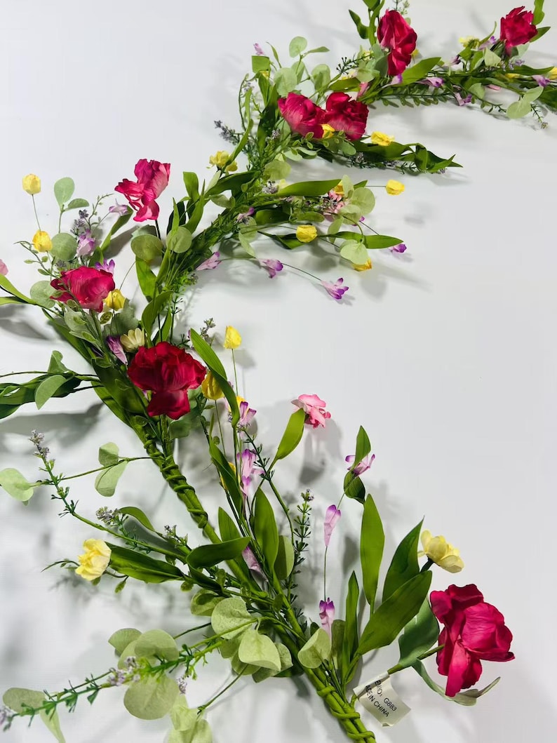 May include: A pink and green floral garland with small pink, yellow, and purple flowers. The garland is made of artificial flowers and greenery.