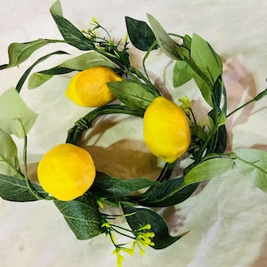 May include: A lemon wreath with three yellow lemons and green leaves. The wreath is made of a wire base and is decorated with artificial lemons and leaves.