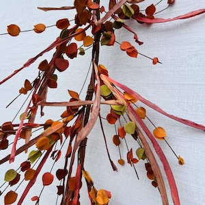 May include: A fall-themed garland with long, thin, red, orange, and brown strips of fabric and small, round, green, orange, and red paper leaves.