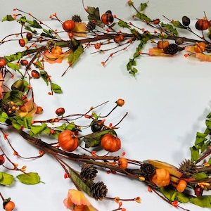 May include: A fall garland with orange and brown pumpkins, green leaves, and red berries. The garland is made of artificial materials and is perfect for decorating for the fall season.