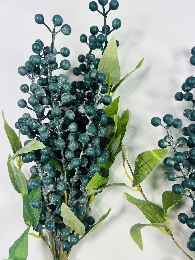 May include: A bunch of faux greenery with dark green berries and leaves. The berries have a frosted look.