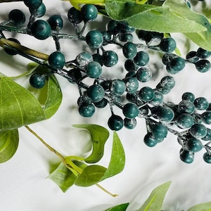 May include: A sprig of faux greenery with dark green berries and leaves. The berries have a frosted look.