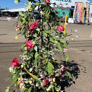 May include: A metal floral stand with a star-shaped base is decorated with pink and white flowers and green leaves. The stand is in front of a building with the word "TRADE" on it.