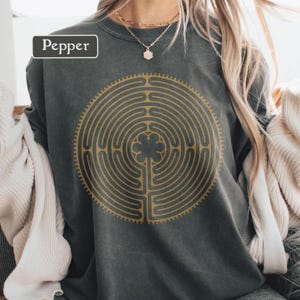 Puede incluir: Sudadera gris oscuro con un diseño de laberinto dorado. El diseño está centrado en la parte delantera y presenta un patrón circular con un trébol de cuatro hojas en el centro. La palabra "Pepper" está en un cuadro blanco en la esquina superior izquierda.