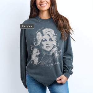 Op de afbeelding: Een antracietgrijs sweatshirt met lange mouwen en ronde hals, voorzien van een grote, vervaagde witte grafische print van een vrouw met volumineus haar op de voorzijde. De tekst Pepper staat in een klein wit kader linksboven.