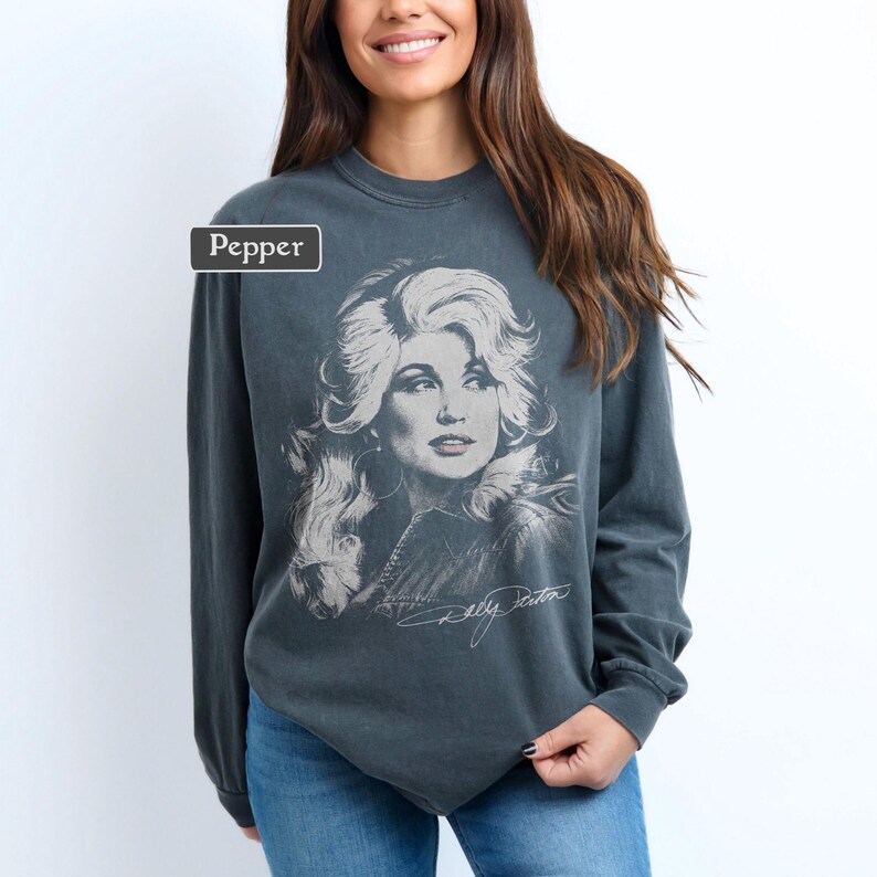 Op de afbeelding: Een antracietgrijs sweatshirt met lange mouwen en ronde hals, voorzien van een grote, vervaagde witte grafische print van een vrouw met volumineus haar op de voorzijde. De tekst Pepper staat in een klein wit kader linksboven.