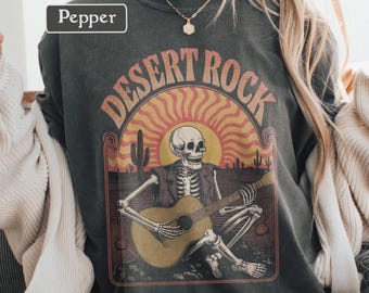 Camiseta gráfica vintage de rock desértico, colores cómodos, top retro con guitarra de esqueleto, estilo bohemio occidental, género de rock desértico para festivales.