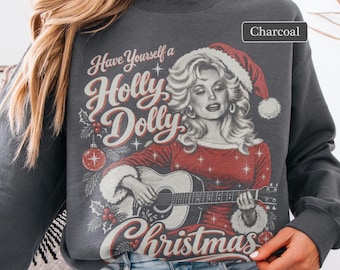 Op de afbeelding: Een antracietkleurige sweater met ronde hals en een grafische print van een blonde vrouw met een kerstmuts die op een akoestische gitaar speelt. De tekst luidt Have Yourself a Holly Dolly Christmas.