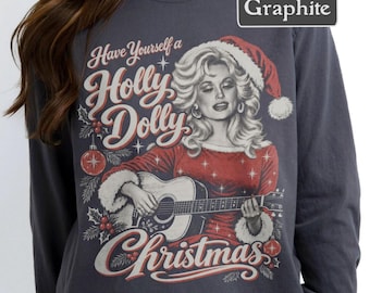 Op de afbeelding: Een antracietkleurig shirt met lange mouwen en een afbeelding van een blonde vrouw met een kerstmuts die op een akoestische gitaar speelt. De tekst luidt Have Yourself a Holly Dolly Christmas, omringd door hulstbessen en kerstballen.