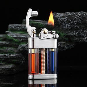 Op de afbeelding: Een zilverkleurige aansteker met een vlam. De aansteker heeft een rechthoekige behuizing met transparante secties met oranje en blauwe vloeistoffen. Het bovenste mechanisme is zilver met gouden accenten.