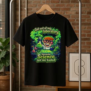 May include: Black t-shirt featuring a cartoon scientist in a lab setting. The design includes the text "Get out of my laboratory" and "because Science got me faded" in a colorful, comic style. The shirt is hanging on a metal clothing rack.