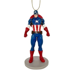May include: A Captain America figurine, featuring a blue and red costume with a white star on the chest. The figurine has a red shield on the back and is mounted on a gray base. The figure is approximately 5 inches tall.