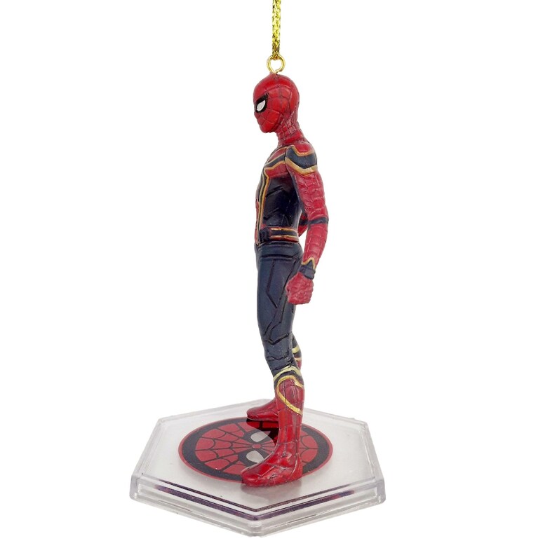 May include: A Spider-Man figurine in a red and black suit with gold accents. The figure is standing on a clear, hexagonal base with a Spider-Man logo. A gold string is attached for hanging.